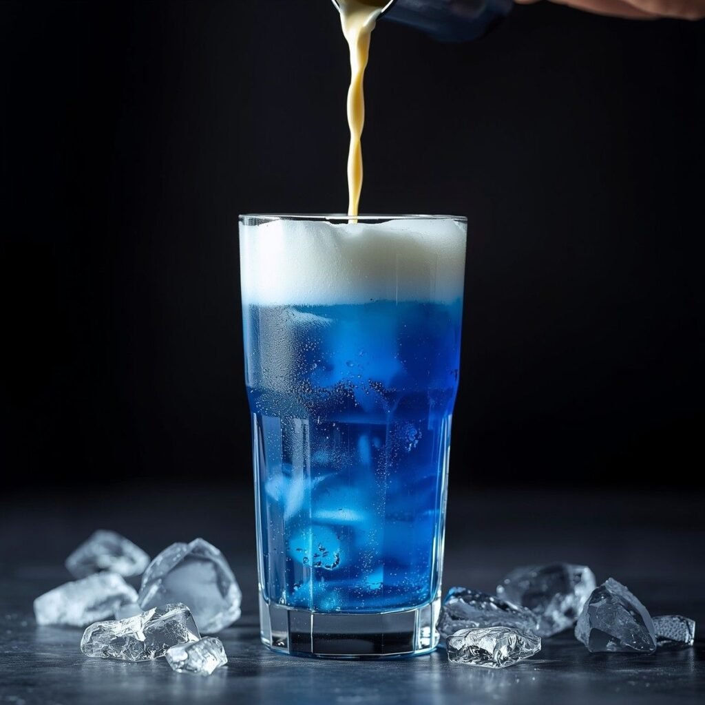 Iced Butterfly Pea Flower Tea Latte being layered over ice with vanilla cold foam on top in drink assembly stage